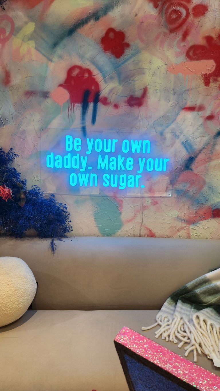 A neon sign that says "Be your own daddy. Make your own sugar."